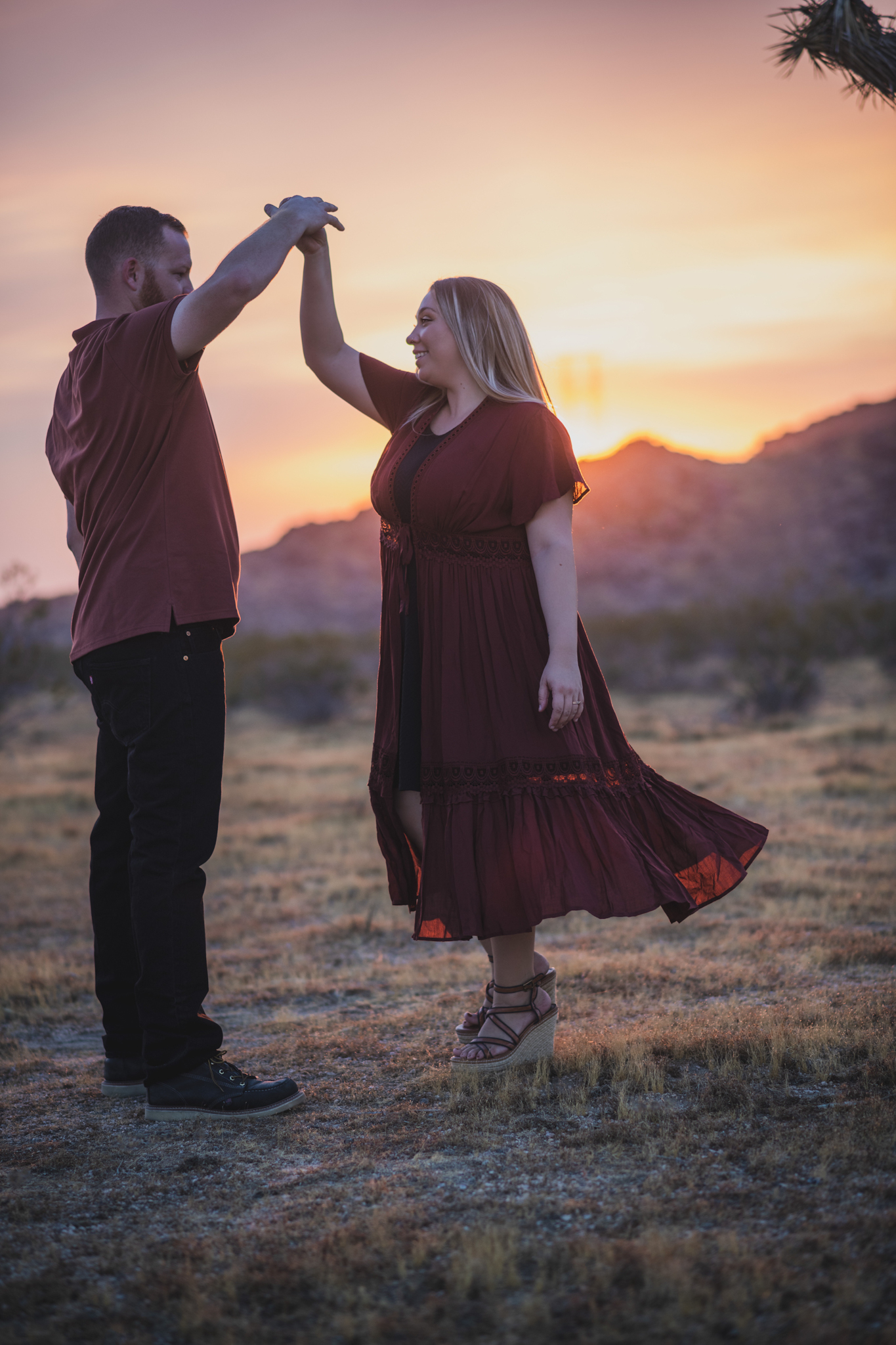 Dark and moody family portraits taken at sunset in the beautiful california mountains in lucerne valley. The high desert sky is behind the mother and father who are wearing red. The three year old daughter is smiling at the high deserts best family photographer