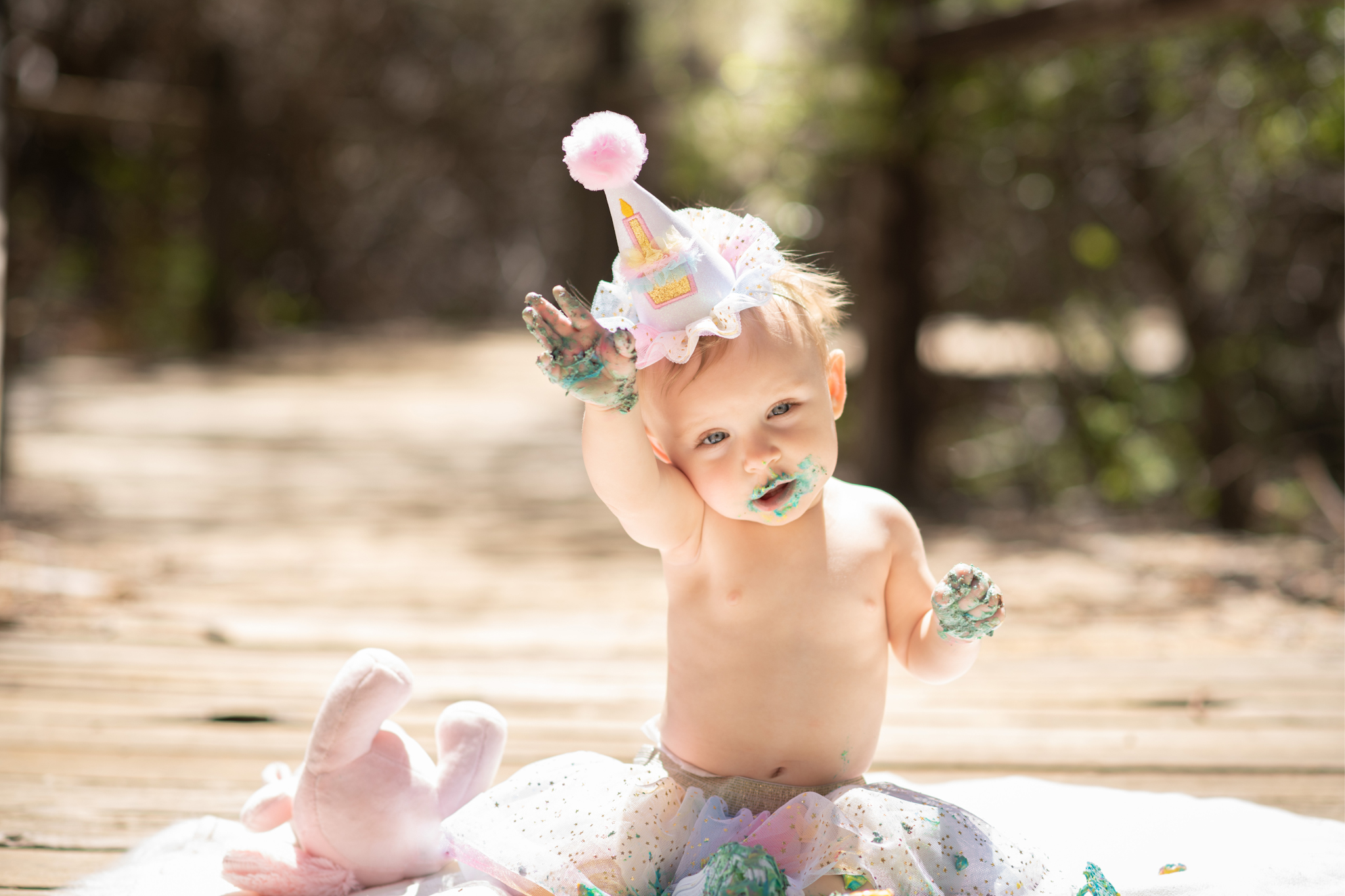 Light and airy pictures of a baby girl sitting on a magical bridge in the mountains of Wrightwood California. Baby is smashing a colorful cake and smearing it on her face in these high desert portraits